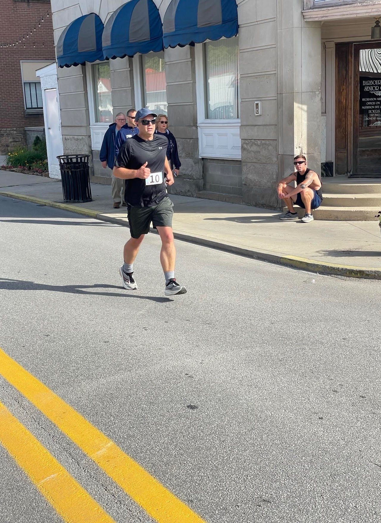 A runner in a black shirt and number 10 races down a city street, with spectators watching nearby.