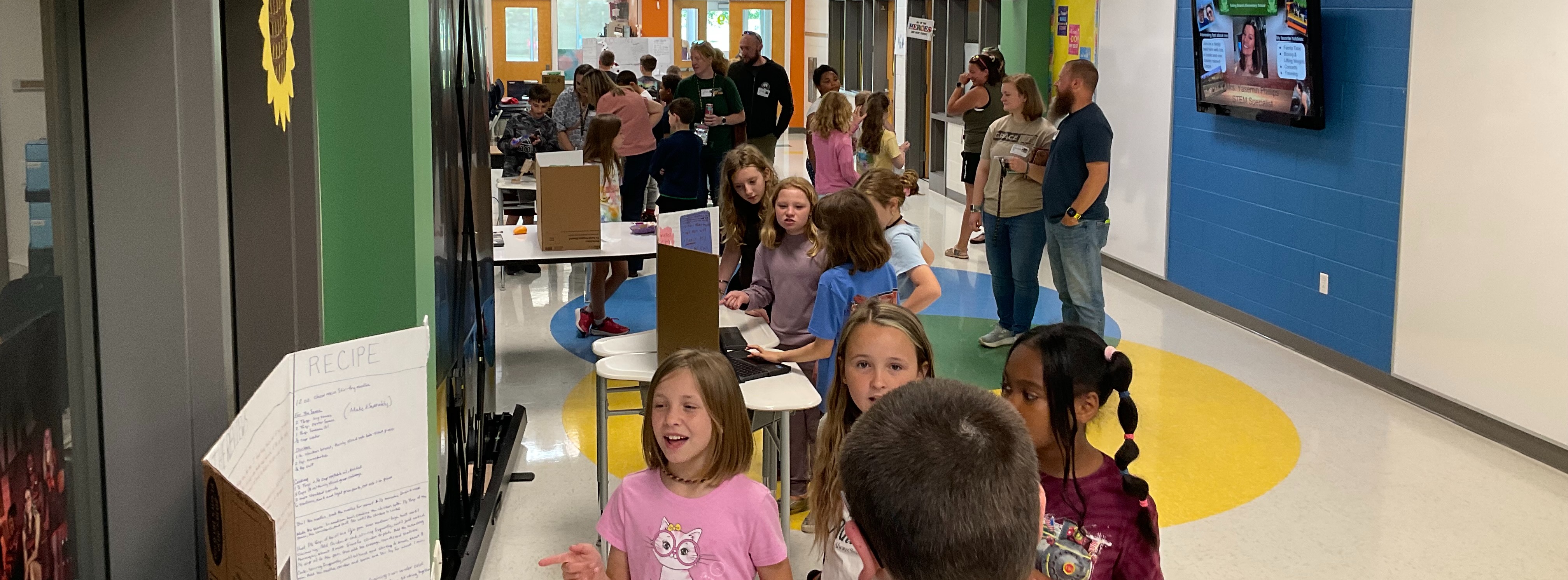 elementary school hallway with many 4th and 5th grade students presenting their passion projects to small groups of students and adults