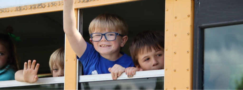 student waving out the window of a school bus