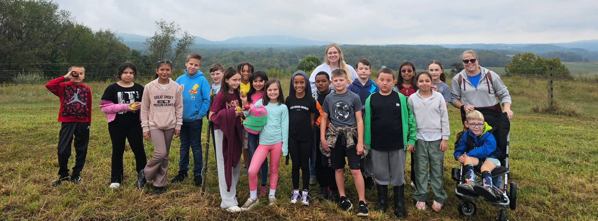 students on a field trip, standing holding apples; mountains in the background