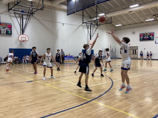 A youth basketball game in progress, with players in motion on the court as one player shoots the ball while others defend.