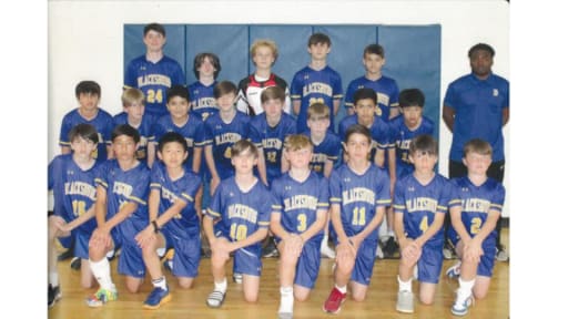 A group photo of a youth sports team, featuring boys in blue jerseys with numbers, posing together in a gymnasium.