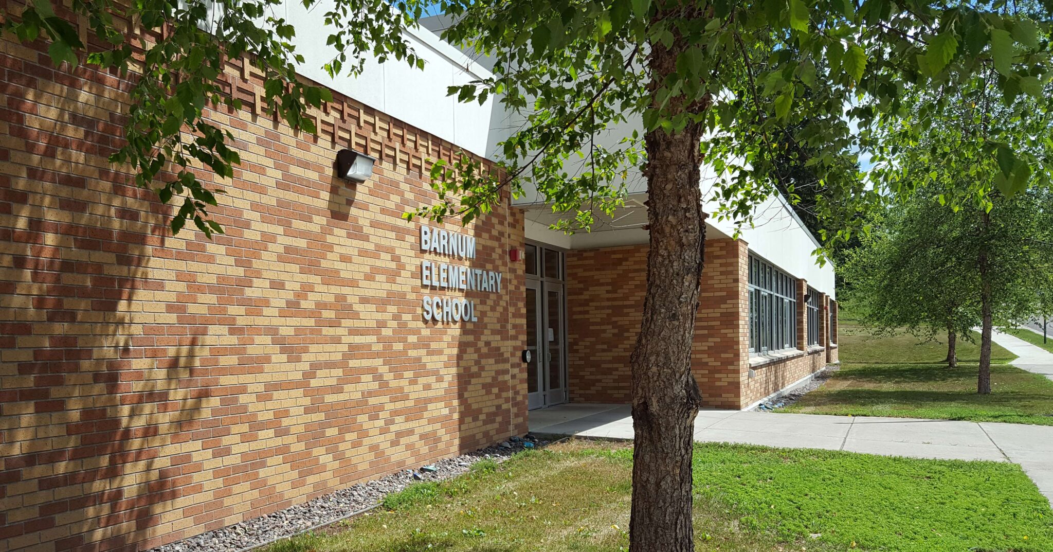 A brick building stands prominently, with a lush tree providing shade in front of it.