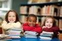 Three children are seated at a table, engaged with various books, showcasing a moment of learning and collaboration.
