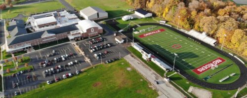 Aerial view showcasing a football field surrounded by a parking lot, highlighting the layout and surrounding area.