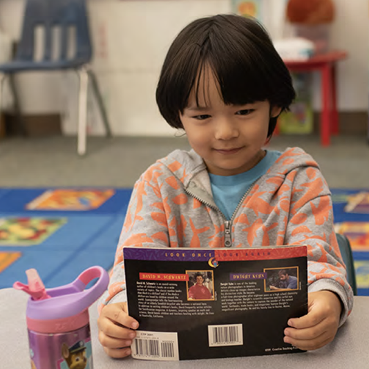 Kindergarten student in a classroom reading a book
