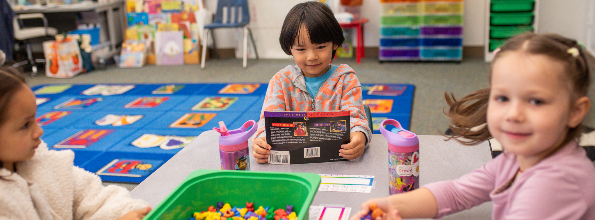 Children participating in a classroom learning activity at a table.
