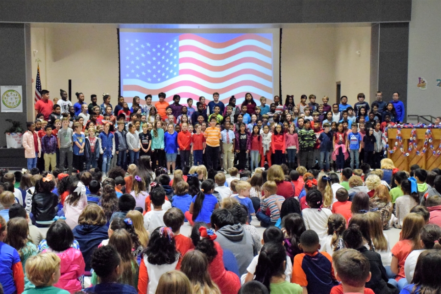 A diverse group of children proudly standing together in front of a large American flag.