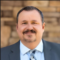 A man in a suit and tie smiles confidently at the camera, exuding professionalism and approachability.