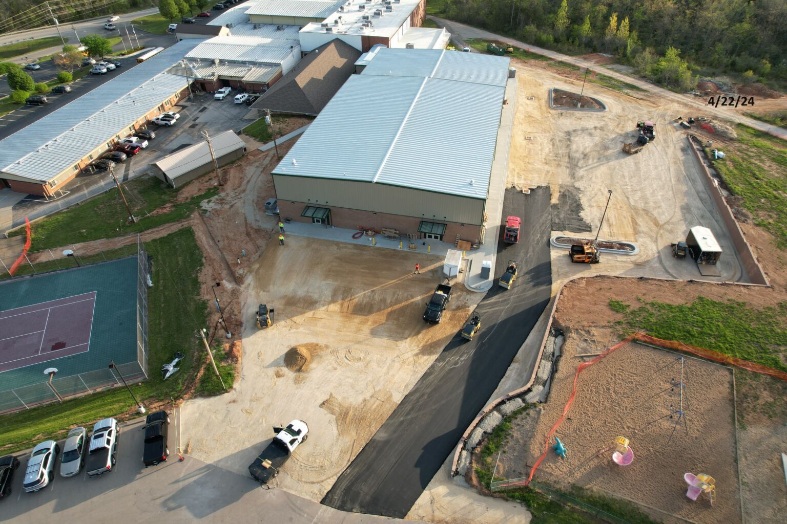 Aerial view of a school building featuring a tennis court, showcasing the layout and surrounding area from above.