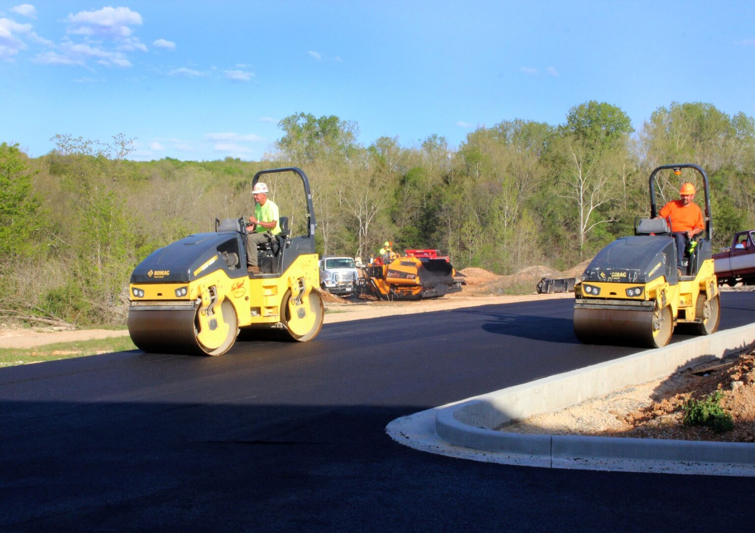 Two men are collaborating on a road construction project, focused on their tasks and surrounded by construction equipment.