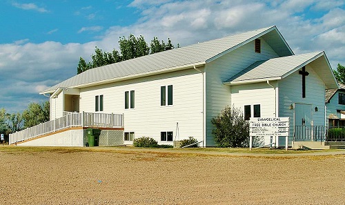 A white church featuring a large white roof, surrounded by a pristine white fence, set against a clear sky.