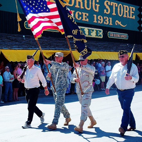 Three men in military uniforms march down the street, proudly carrying flags.