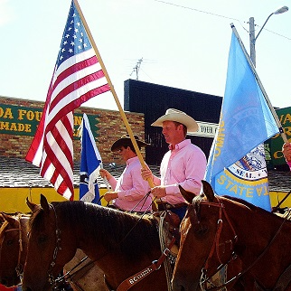 A diverse group of individuals riding horses, showcasing a vibrant parade atmosphere with colorful decorations and spectators.