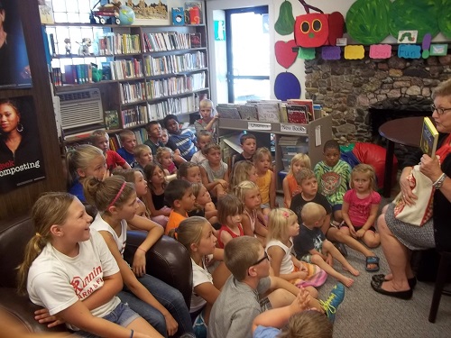A woman reading a story to a group of attentive children in a cozy library setting.