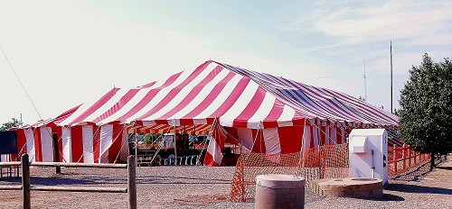 A red and white striped tent stands beside a wooden fence, creating a vibrant outdoor scene.