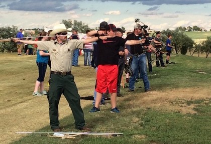 A man wearing a cowboy hat stands confidently, holding a bow and arrow, ready for action in a rustic setting.