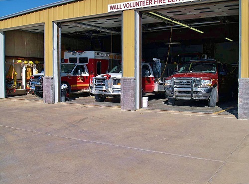 Three fire trucks parked in a garage, with a ladder truck visible in the background, ready for emergency response.