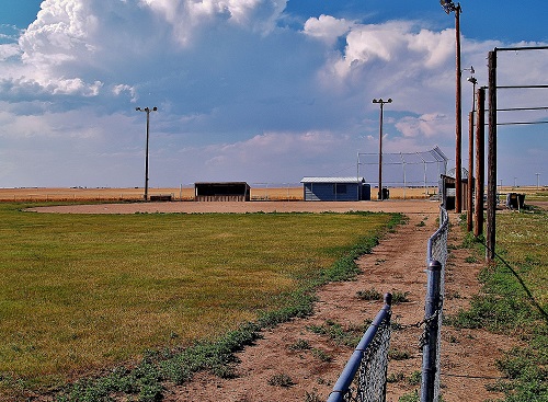 A baseball field featuring a diamond layout, surrounded by a fence, under a clear blue sky.