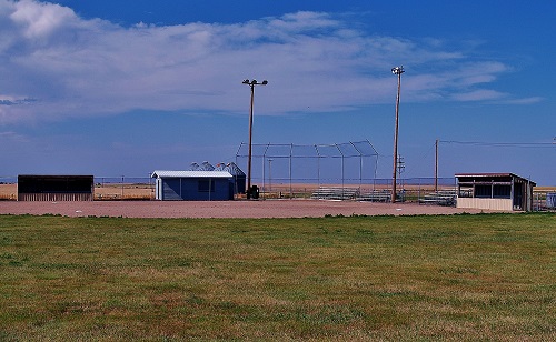 A baseball field featuring a surrounding fence and a light pole, set against a clear sky.