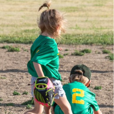 Two young children in green uniforms joyfully playing baseball on a sunny day in a grassy field.