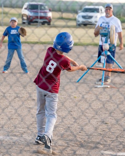 A young boy swings a baseball bat, aiming at a ball in a sunny outdoor setting.