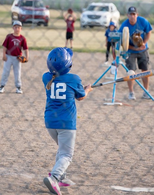 A young boy energetically swings a baseball bat, aiming at a ball in a sunny outdoor setting.