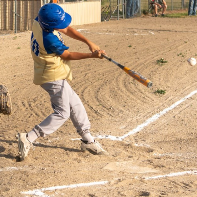 A young boy swings a baseball bat, aiming at a ball in mid-air, showcasing his enthusiasm for the game.