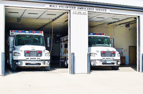Two ambulances parked inside a garage adjacent to a white building, showcasing emergency medical services readiness.