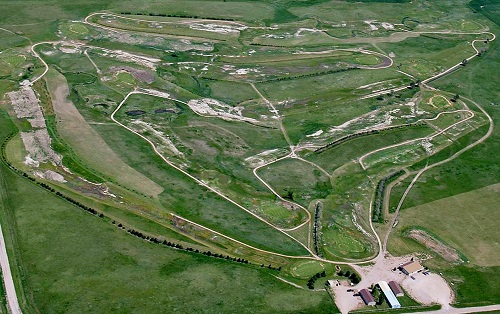 Aerial view of a golf course featuring lush greens, a winding road, and a track, showcasing the landscape's beauty.
