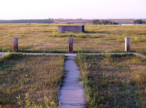 A serene path winding through a grassy field, leading to a charming water fountain in the distance.
