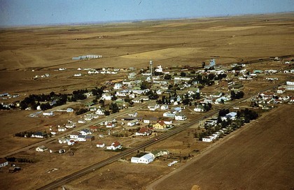 Aerial view of a quaint small town surrounded by expansive green fields under a clear blue sky.