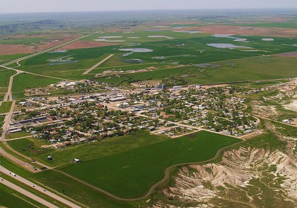 Aerial view of a quaint small town surrounded by expansive green fields under a clear blue sky.