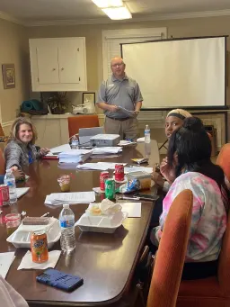 A diverse group of individuals engaged in discussion around a table covered with papers and documents.