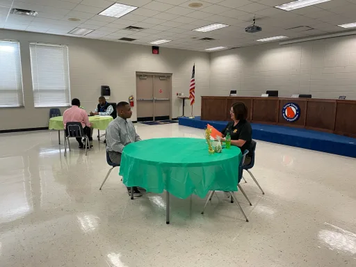A diverse group of individuals seated at tables, engaged in conversation within a well-lit room.