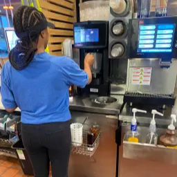 A woman in a blue shirt stands confidently in front of a machine, showcasing her engagement with the equipment.