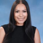 A smiling young woman with long dark hair, wearing a black sleeveless top, poses against a blue background.
