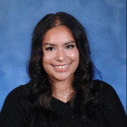 A smiling young woman with long dark hair, wearing a black sleeveless top, poses against a blue background.