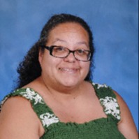 A smiling woman with curly hair and glasses is wearing a maroon shirt with a heart design, set against a light blue background.