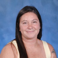 A woman with long, straight hair and earrings smiles at the camera, wearing a striped shirt against a blue background.