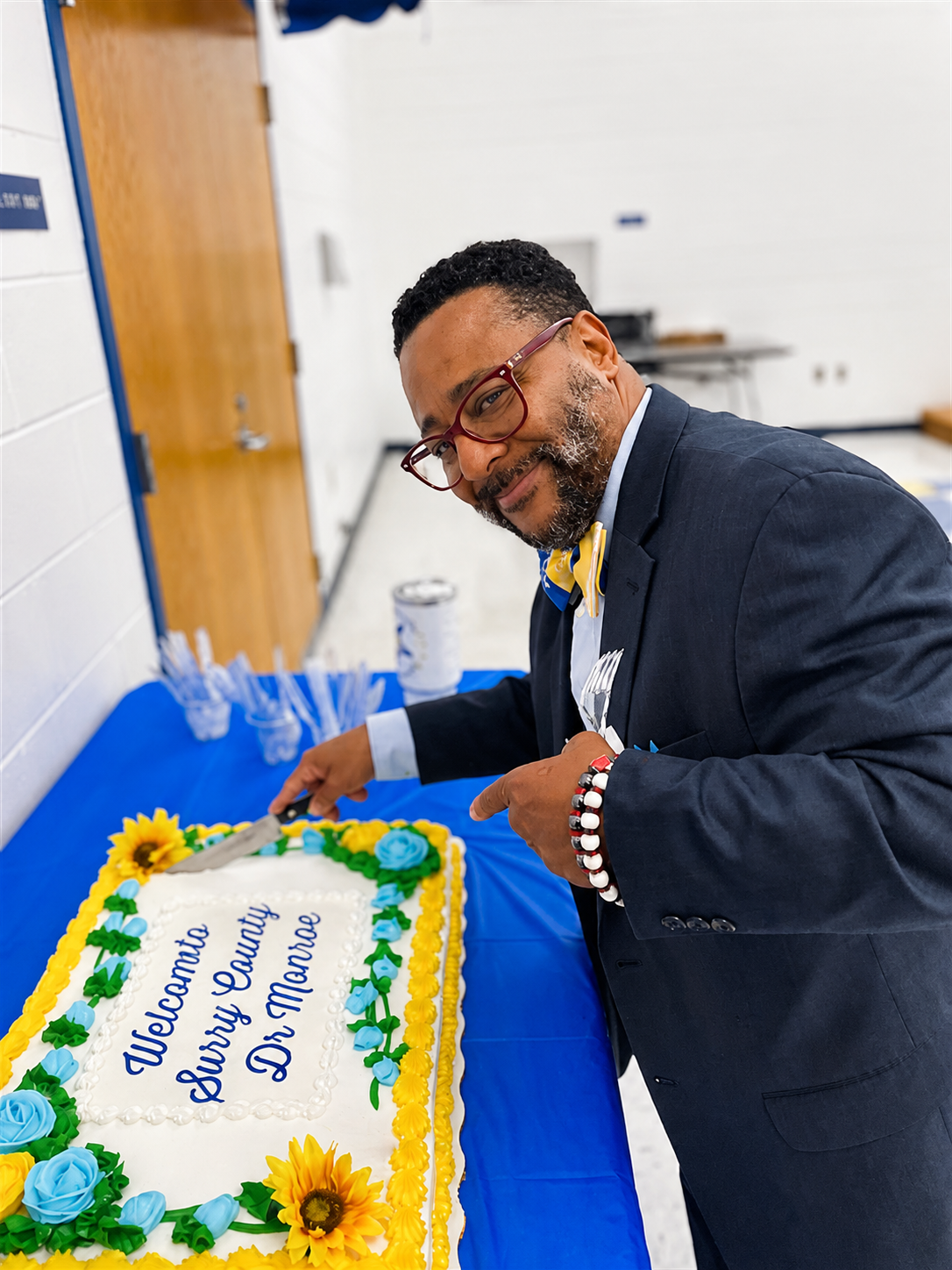 School administrator smiling while preparing to cut a decorated welcome cake at a school celebration.