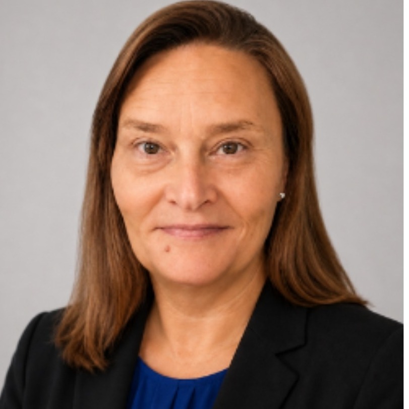 Professional head-and-shoulders portrait of a woman with shoulder-length brown hair wearing a black blazer over a royal blue blouse. She is facing the camera with a slight smile against a soft gray studio background.