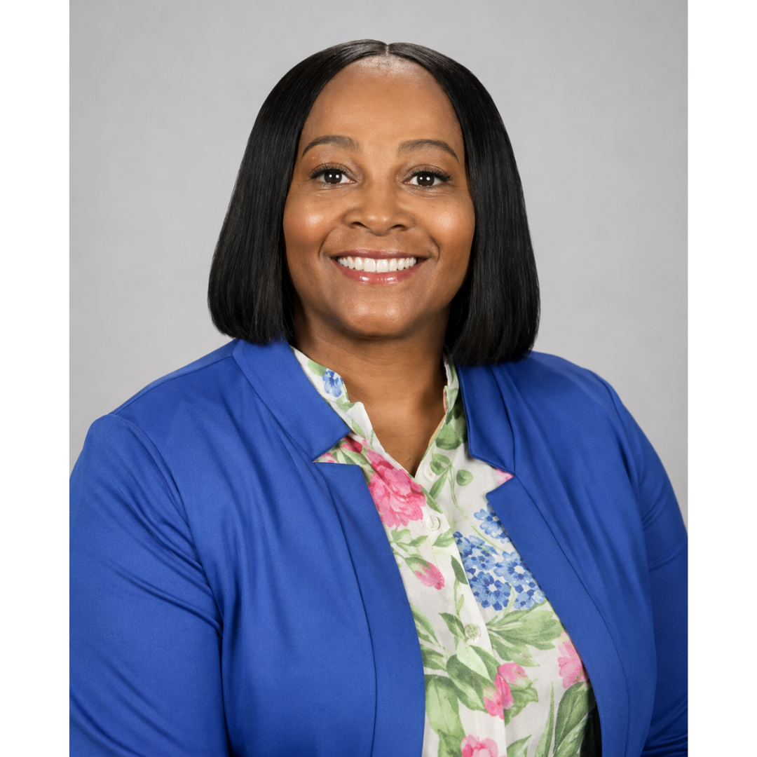 Professional headshot of a smiling woman wearing a royal blue blazer over a floral blouse against a light gray background.