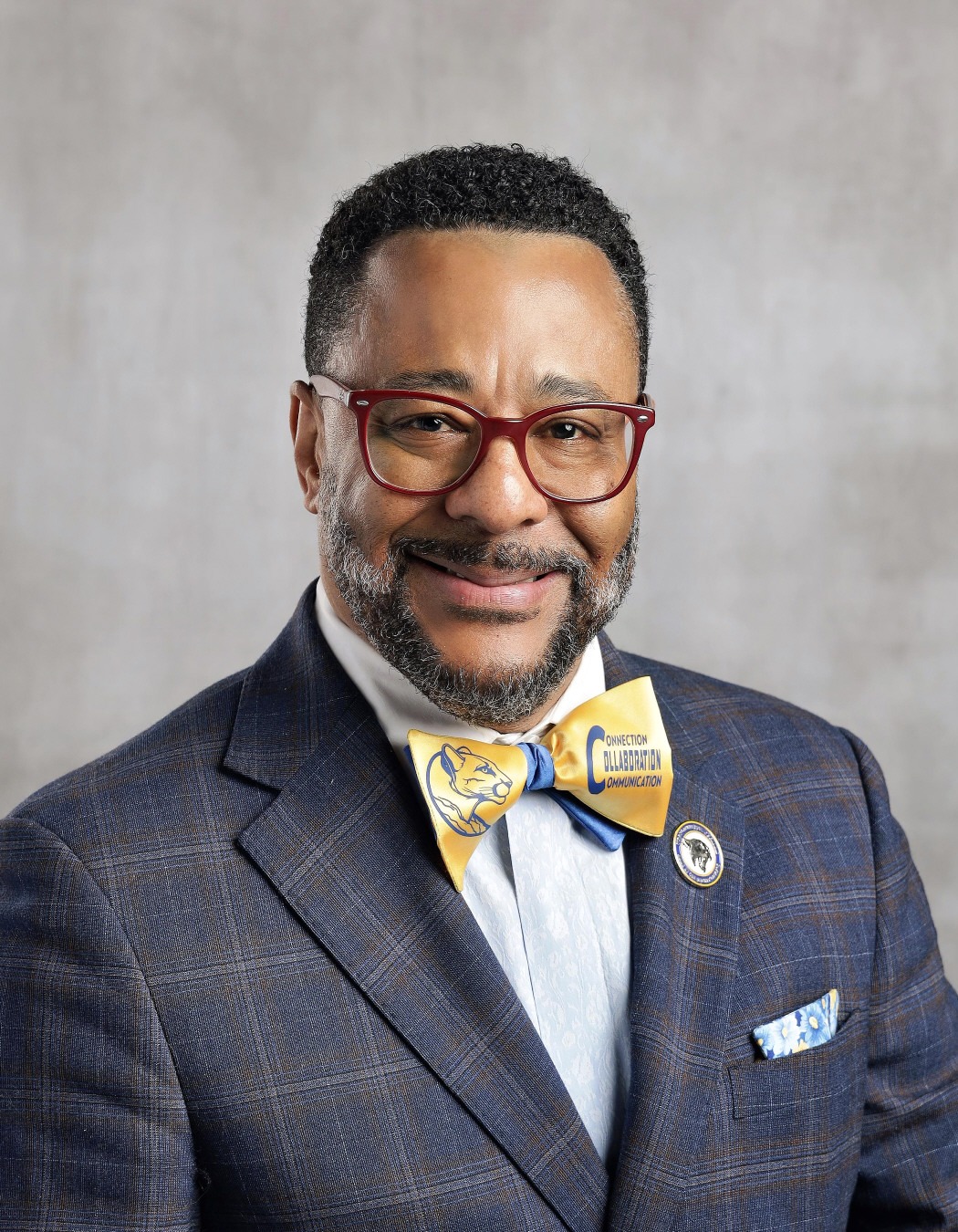 Dr. Herbert Monroe: Professional portrait of a smiling man wearing red glasses, a navy suit, and a blue-and-gold bow tie featuring a cougar logo.