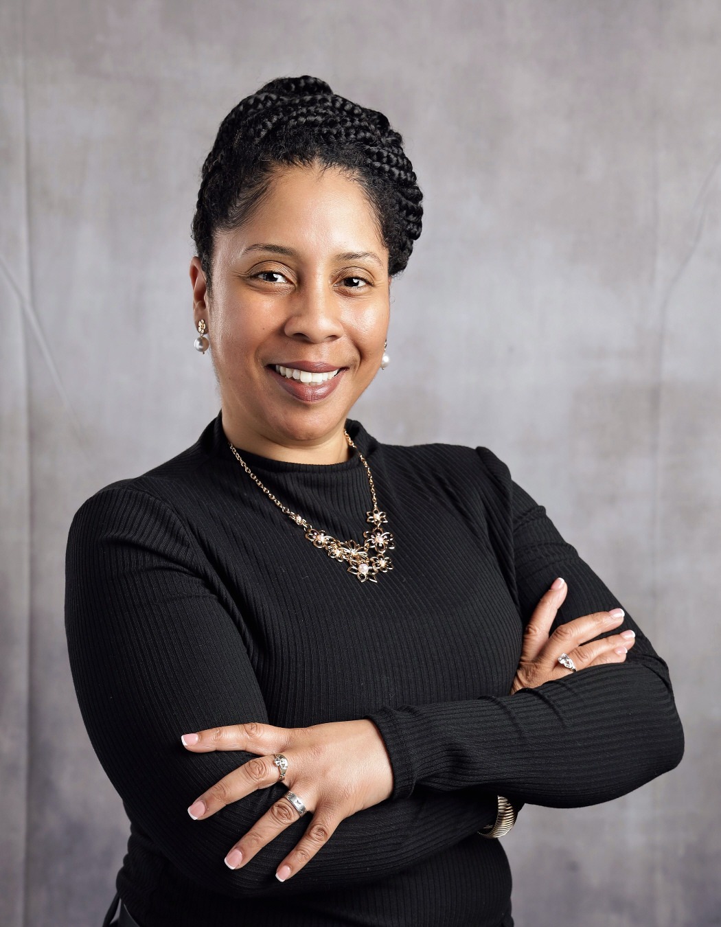 Renita Bailey: Professional portrait of a smiling woman wearing a black top and gold necklace with her arms crossed.