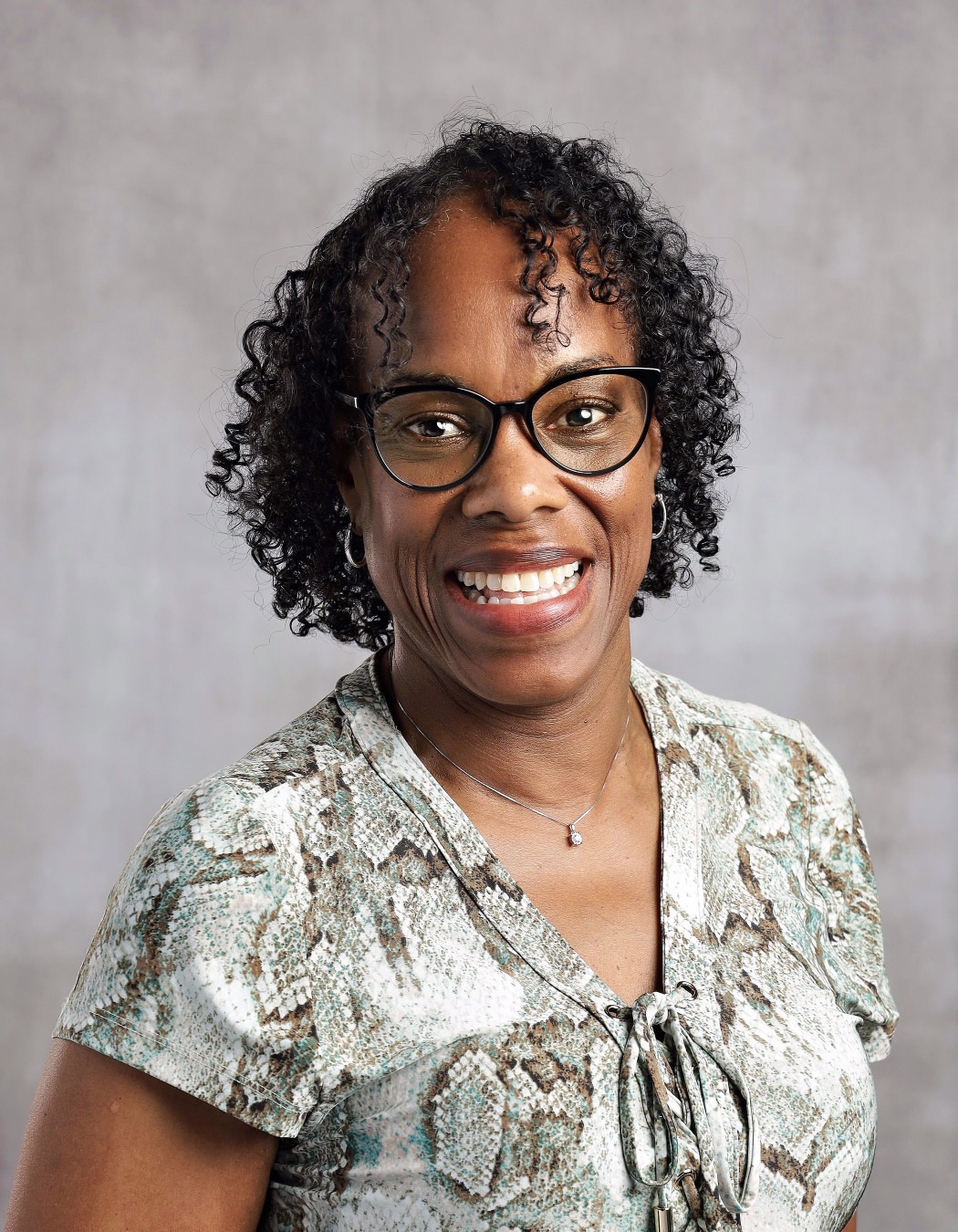Vonda Thomas: Professional portrait of a smiling woman wearing black glasses and a patterned blouse.