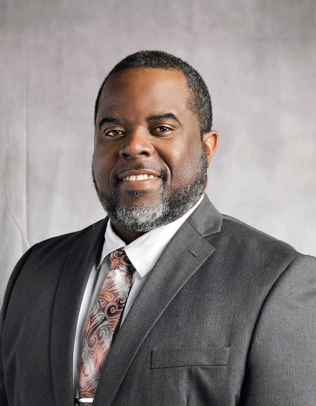 James Pope: Professional portrait of a smiling man wearing a gray suit, white shirt, and patterned tie.