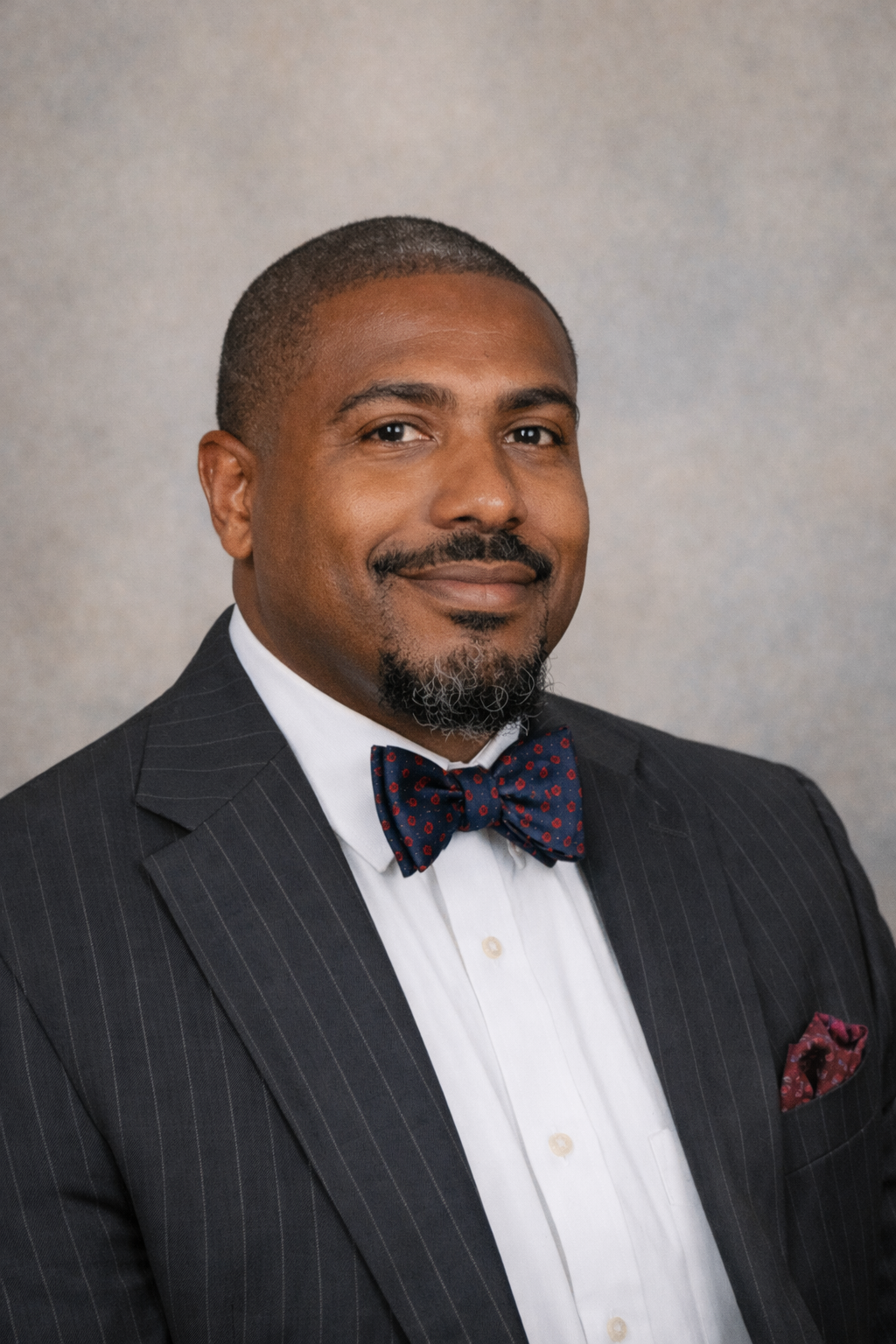 Aaron Harris: Professional portrait of a smiling man wearing a dark pinstripe suit, white shirt, and patterned bow tie.