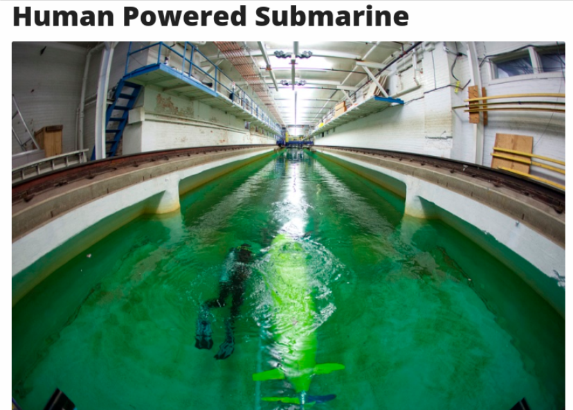 A human-powered submarine is submerged in a testing tank, surrounded by green water and industrial surroundings.