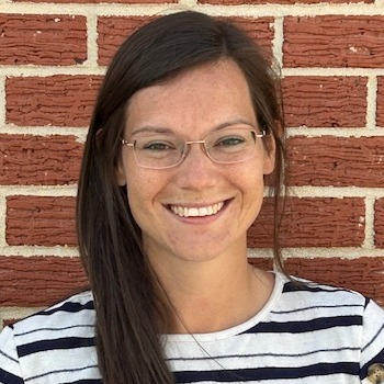 A woman with glasses wearing a plaid shirt, smiling and looking confidently at the camera.